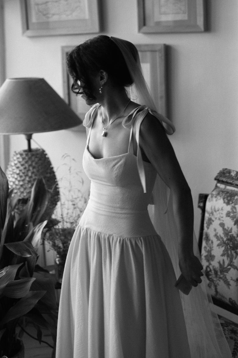 Woman in a white dress standing in a room with framed pictures on the wall.