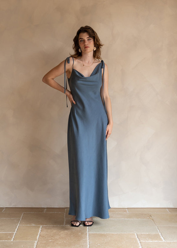 Woman wearing a blue slip dress standing against a plain wall.